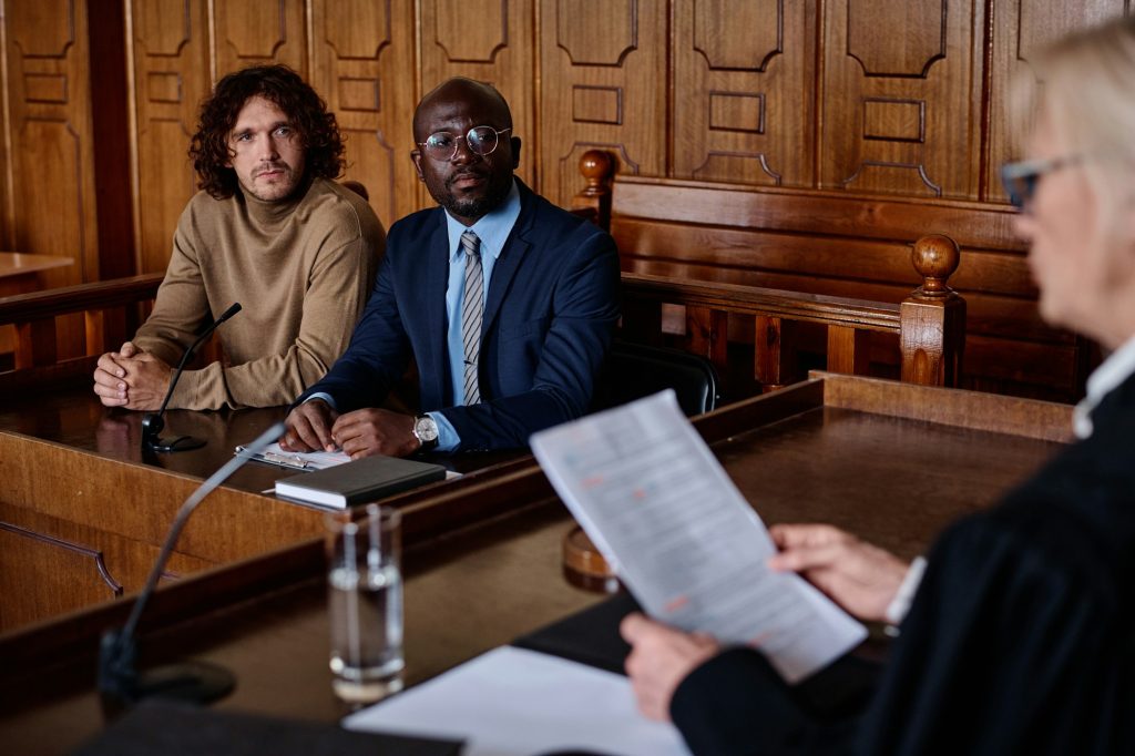 Two young intercultural male attorneys looking at female judge with papers