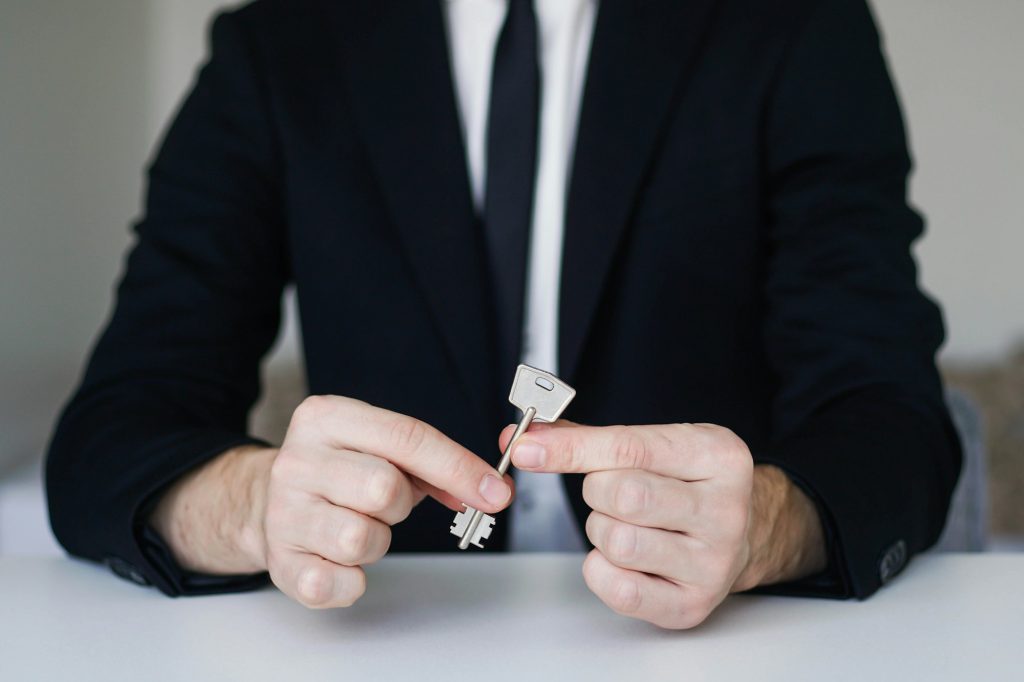 Young man in a suit holding a key from a new apartment in his hand. Realtor, home loan concept.